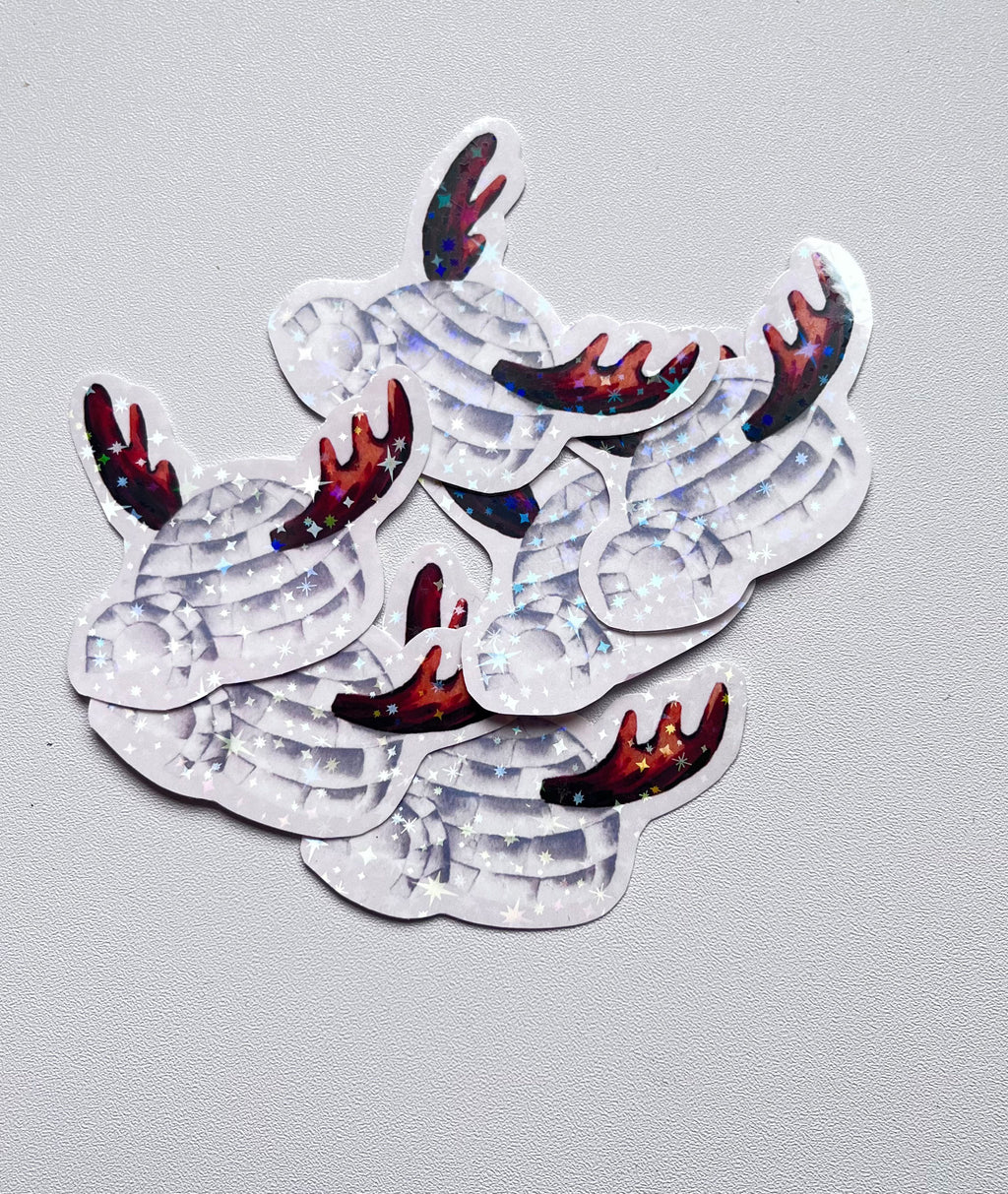 Stickers représentant un igloo gris avec une entrée arrondie et des bois de renne bruns, ornés d’étoiles holographiques, sur un fond gris clair.