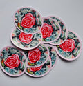Stickers ronds Le Rosier d’hiver, ornés d’une rose rouge et rose sur un feuillage vert et bleu grisé, avec une bordure rose pâle, sur fond gris clair.