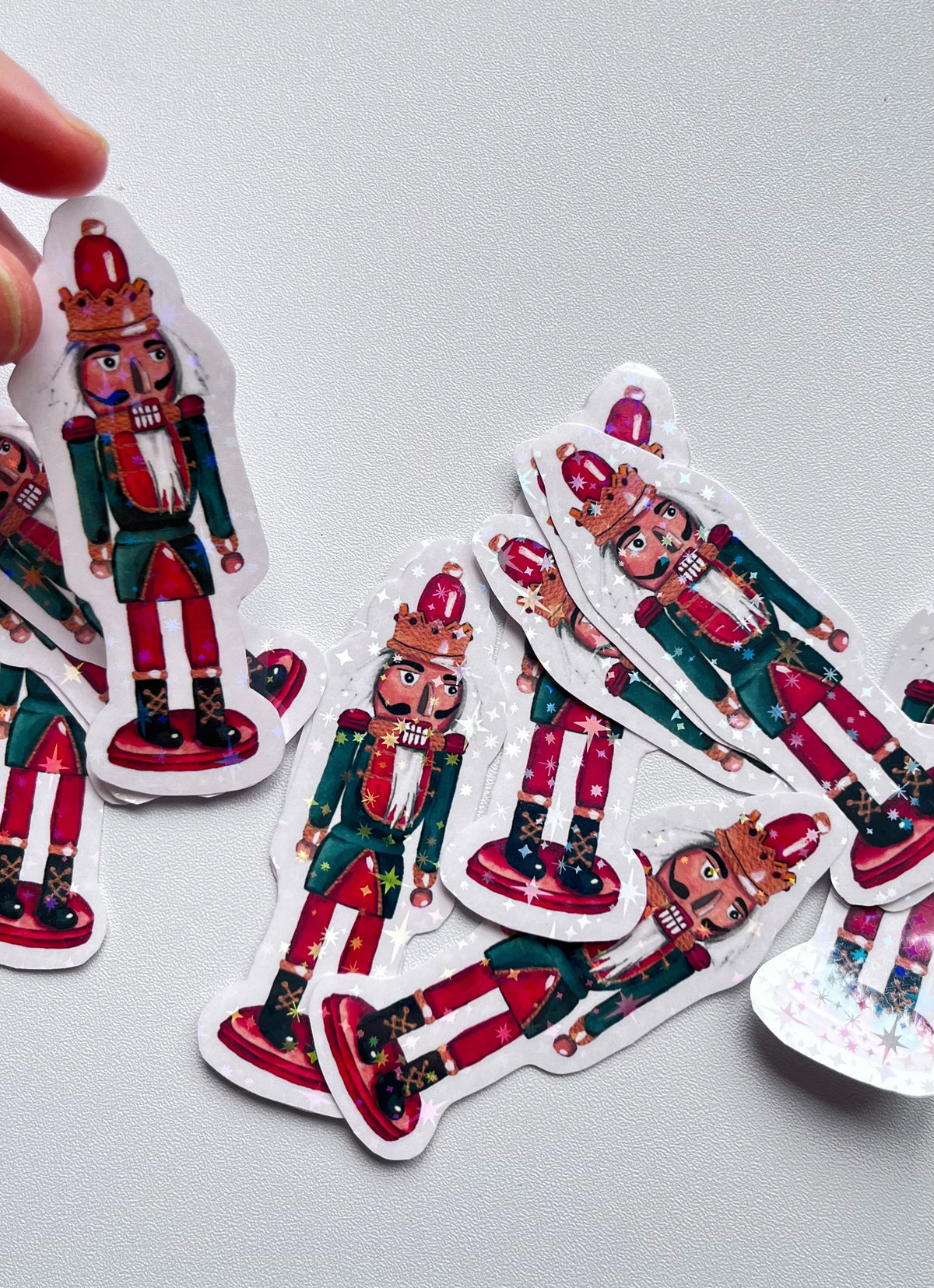 Stickers de Noël représentant un casse-noisette rouge et vert, avec une couronne dorée, une barbe blanche et des reflets étoilés, sur fond gris clair.