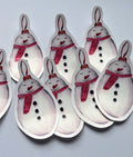 Stickers illustrés en forme de bonhomme de neige souriant avec une écharpe rouge et trois boutons noirs, disposés sur un fond gris clair.
