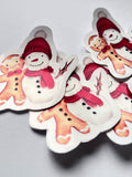 Stickers de Noël représentant un bonhomme de neige à bonnet rouge et écharpe rose aux côtés d’un bonhomme en pain d’épices, sur un fond gris clair.